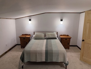 A bedroom with a bed, two nightstands, a wooden door, and two wall-mounted lights.