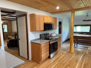 A modern kitchen with wooden cabinets, a microwave, a kettle, and a dining area with a table and chairs.