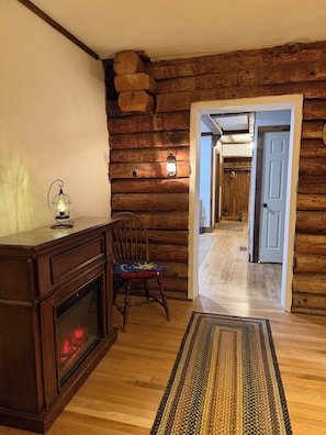 A log cabin interior with a fireplace, a wooden chair, a rug, and a lantern.