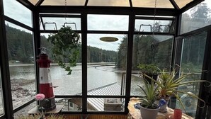 Ein Wintergarten mit Blick auf einen See, einem Leuchtturm-Modell und verschiedenen Kübelpflanzen.