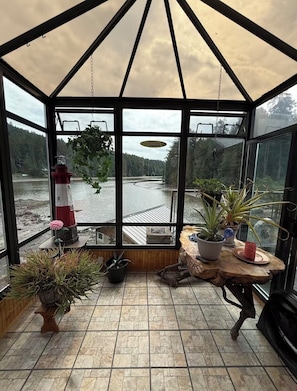 Ein Wintergarten mit Blick auf einen See, einem Leuchtturm-Modell und verschiedenen Kübelpflanzen.