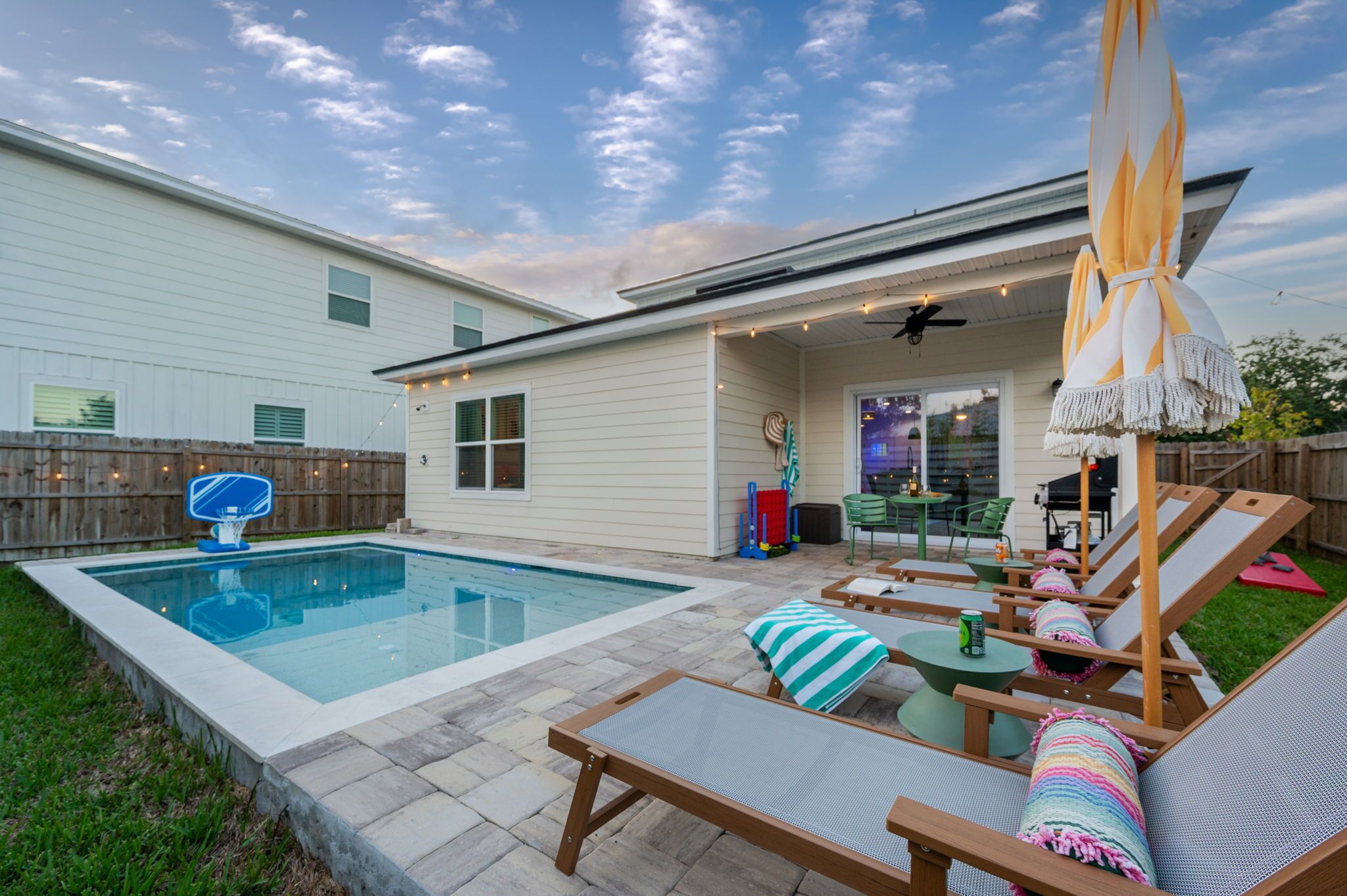 A backyard with a swimming pool, lounge chairs, and a patio area.