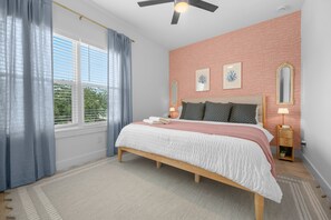 Ein Schlafzimmer mit einem Bett, einem Vorhangfenster, einem Deckenventilator und einem Nachttisch mit Lampe.