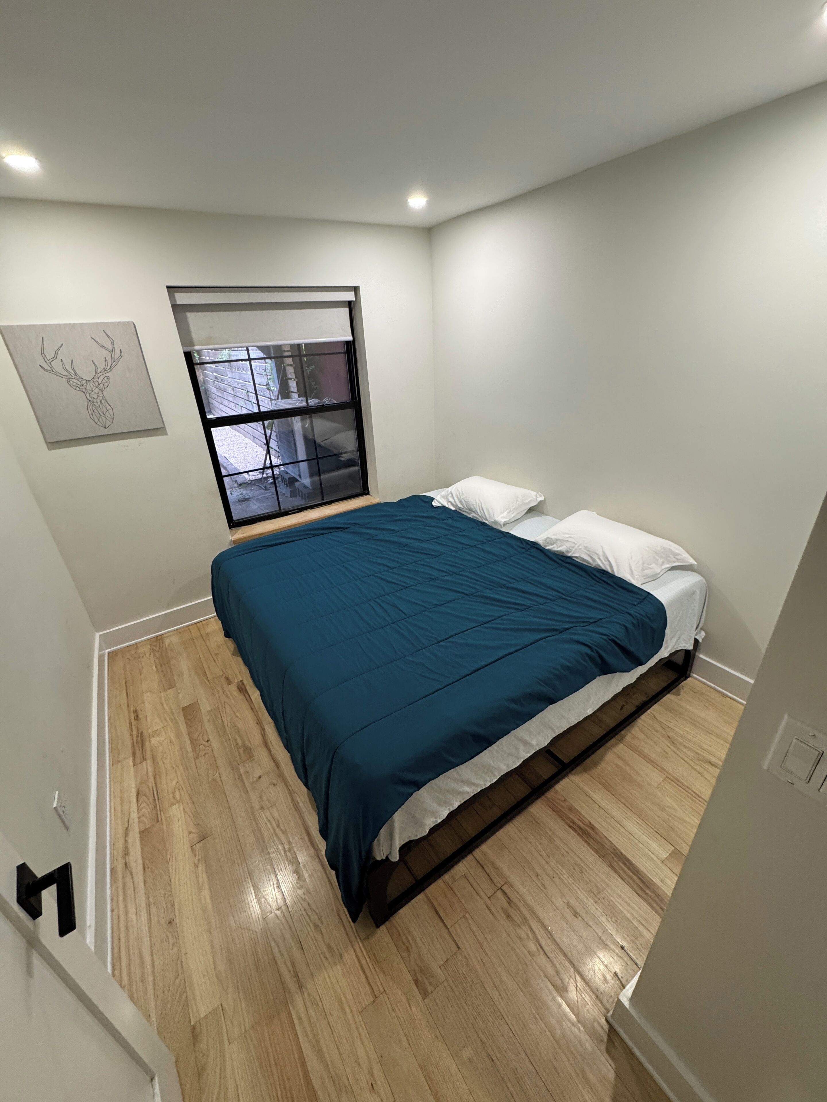 Une chambre à coucher avec un lit, une fenêtre, une porte et un luminaire fixé au mur.