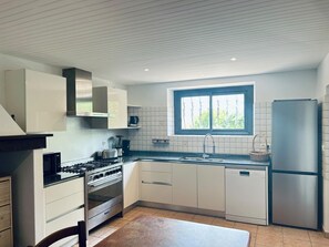Una cuina moderna amb armaris blancs, un frigorífic d'acer inoxidable i una finestra amb vistes a la verdura.