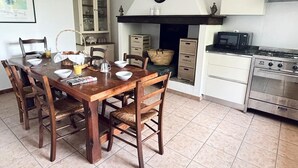 Une cuisine avec une table à manger en bois, des chaises, une cuisinière, des placards et une horloge au mur.