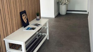 Un espace d’accueil comprenant un banc blanc, un porte-manteau fixé au mur, un tableau encadré et une plante en pot.