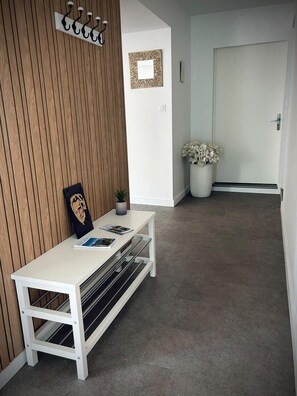 A reception area with a white bench, a wall-mounted coat rack, a framed picture, and a potted plant. - Marcal - Clermont-le-Fort (CLERMONT LE FORT)