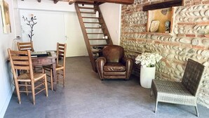 Un intérieur rustique avec un mur en pierre, une table à manger en bois et des chaises, un fauteuil en cuir et un canapé en osier.