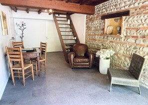 A rustic interior with a stone wall, a wooden dining table with chairs, a leather armchair, and a wicker sofa. - Marcal - Clermont-le-Fort (CLERMONT LE FORT)