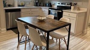 Una cocina moderna con armarios blancos, un lavavajillas de acero inoxidable, un microondas y una mesa de comedor con cuatro sillas.