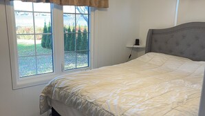 Un dormitorio con cama, ventilador de techo, ventana con cortinas y vistas al exterior.