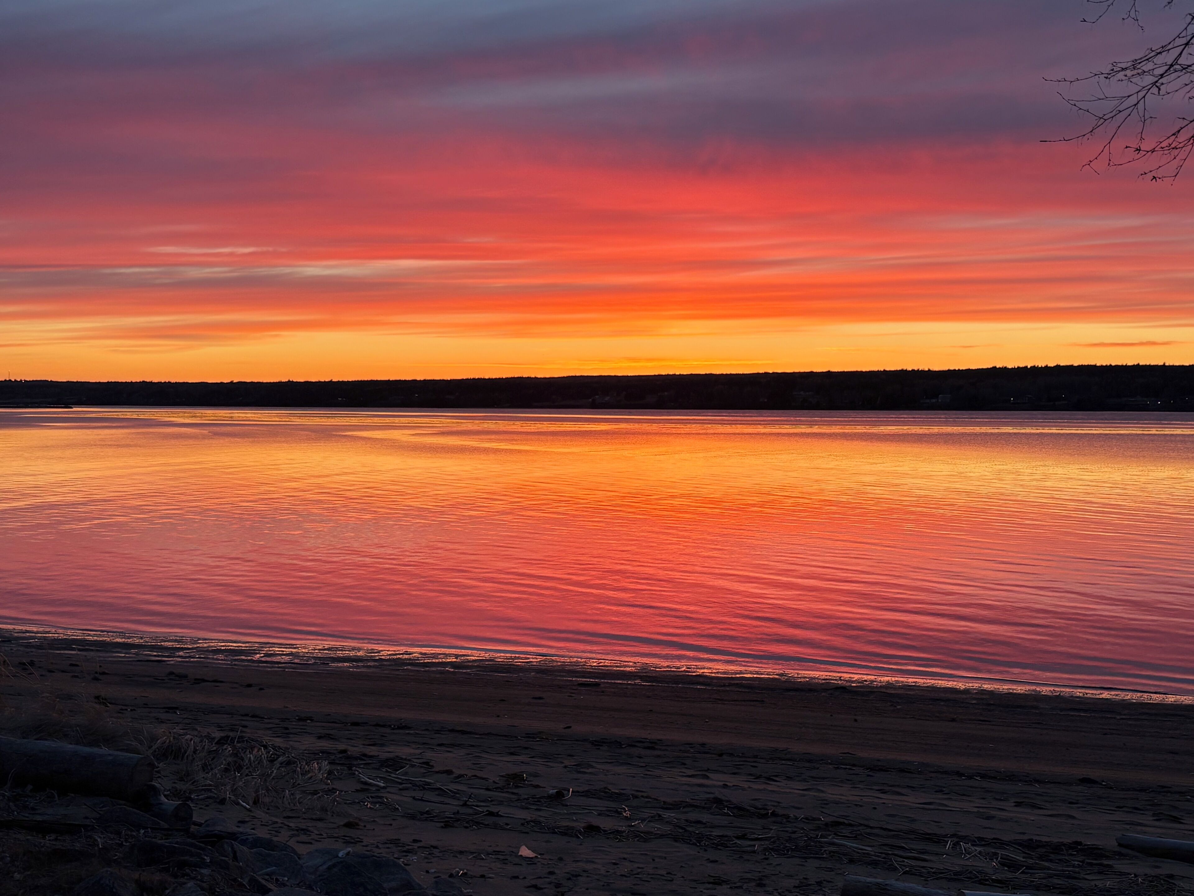 A sunset over a calm body of water with a distant shoreline.