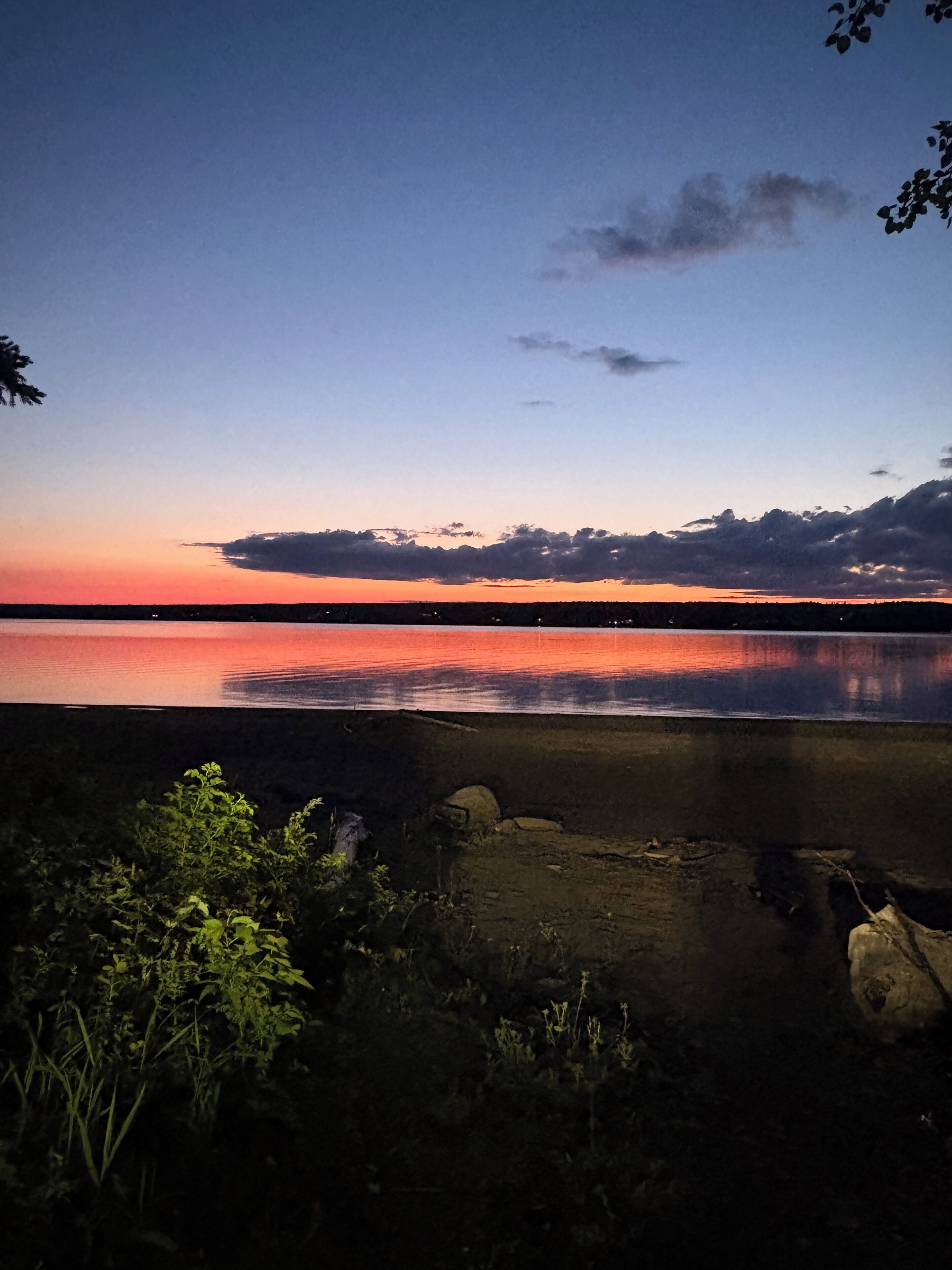 Un lago tranquillo al crepuscolo con cielo sereno, circondato da vegetazione e rocce.