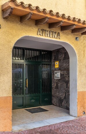 Ein Gebäudeeingang mit einem Schild, das 'ATHENA' zeigt, einem Metallgitter, einer Marmorwand und einem gefliesten Boden.