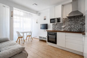 Eine moderne Küche mit weißen Schränken, einer Mikrowelle und einem Herd. Es gibt einen Essbereich mit Tisch und Stühlen sowie ein Sofa im Wohnbereich.