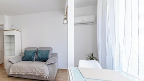 Una habitación con sofá, una mesita, una planta colgante y un equipo de aire acondicionado.