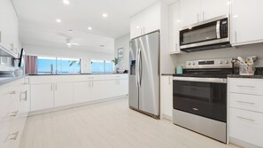 A modern kitchen with white cabinetry, stainless steel appliances, and a view of the ocean. - Casa Caribe #24 - 3 Bed, 3 Bath - Third Floor Ocean Front Panorama Condo (Seven Mile Beach)