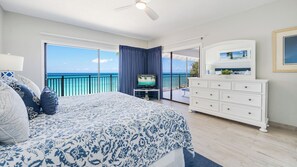Une chambre dotée d’un grand lit, d’une télévision, d’une commode et d’un balcon offrant une vue sur l’océan.