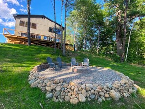 A cabin with a deck, a fire pit, and Adirondack chairs.