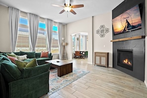 A living room with a green sofa, a coffee table, a fireplace, and a TV mounted on the wall. - Pet Door & Patio, Fort Bliss, North Hills Shopping, Painted Dunes Golf Course (El Paso)