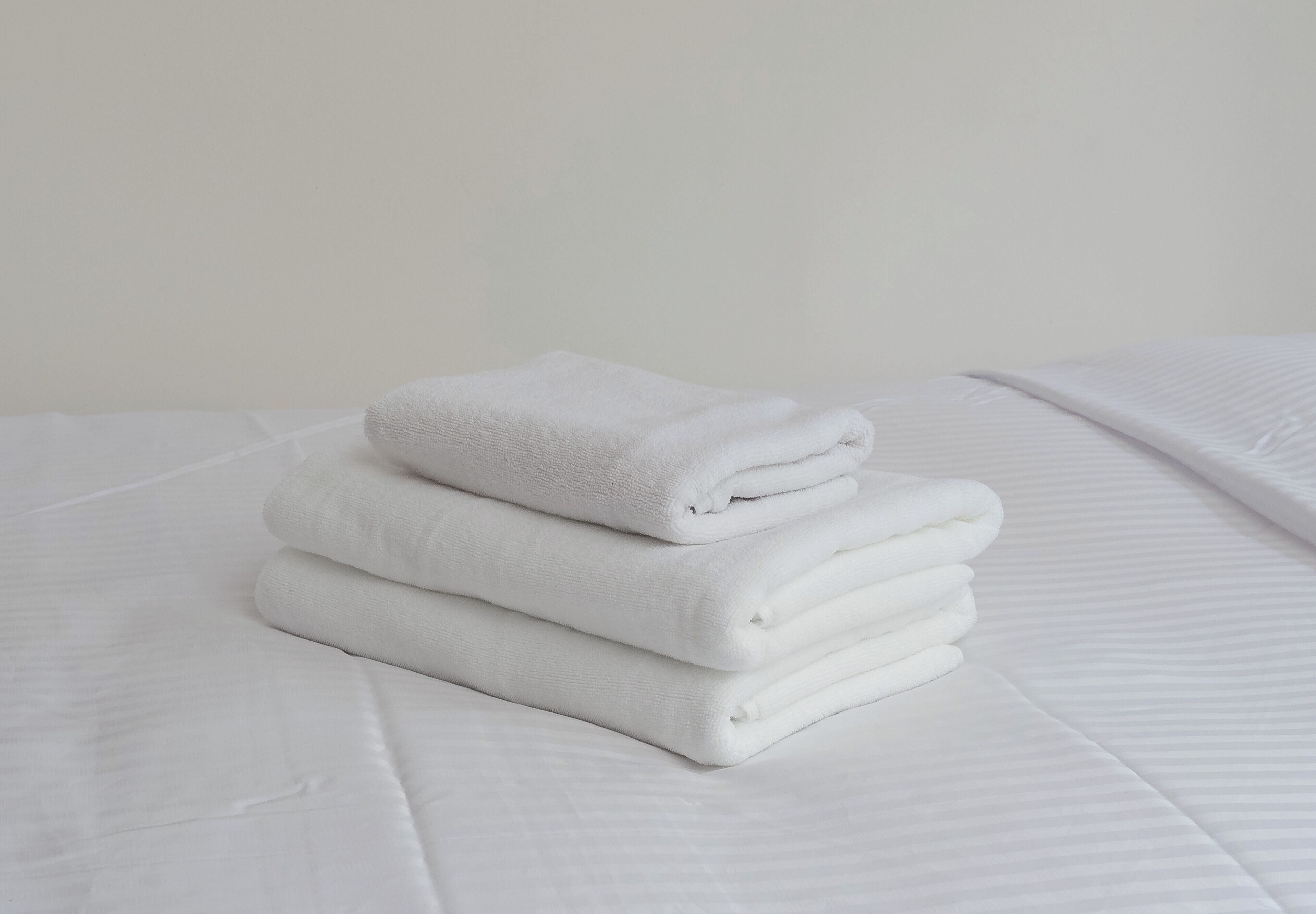 A neatly folded white towel stacked on a white bed with a textured surface.