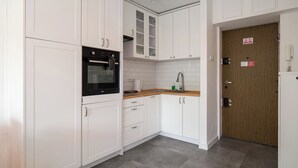 Eine Küche mit weißen Schränken, einem schwarzen Ofen, einer Holz Arbeitsplatte und einer Holztür.