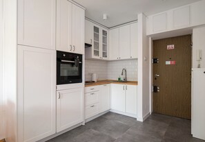 Eine Küche mit weißen Schränken, einem schwarzen Ofen, einer Holz Arbeitsplatte und einer Holztür.