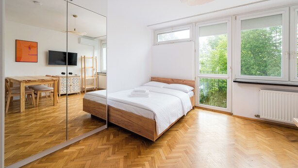Ein Schlafzimmer mit Bett, Fernseher, Schreibtisch und einem großen Fenster.