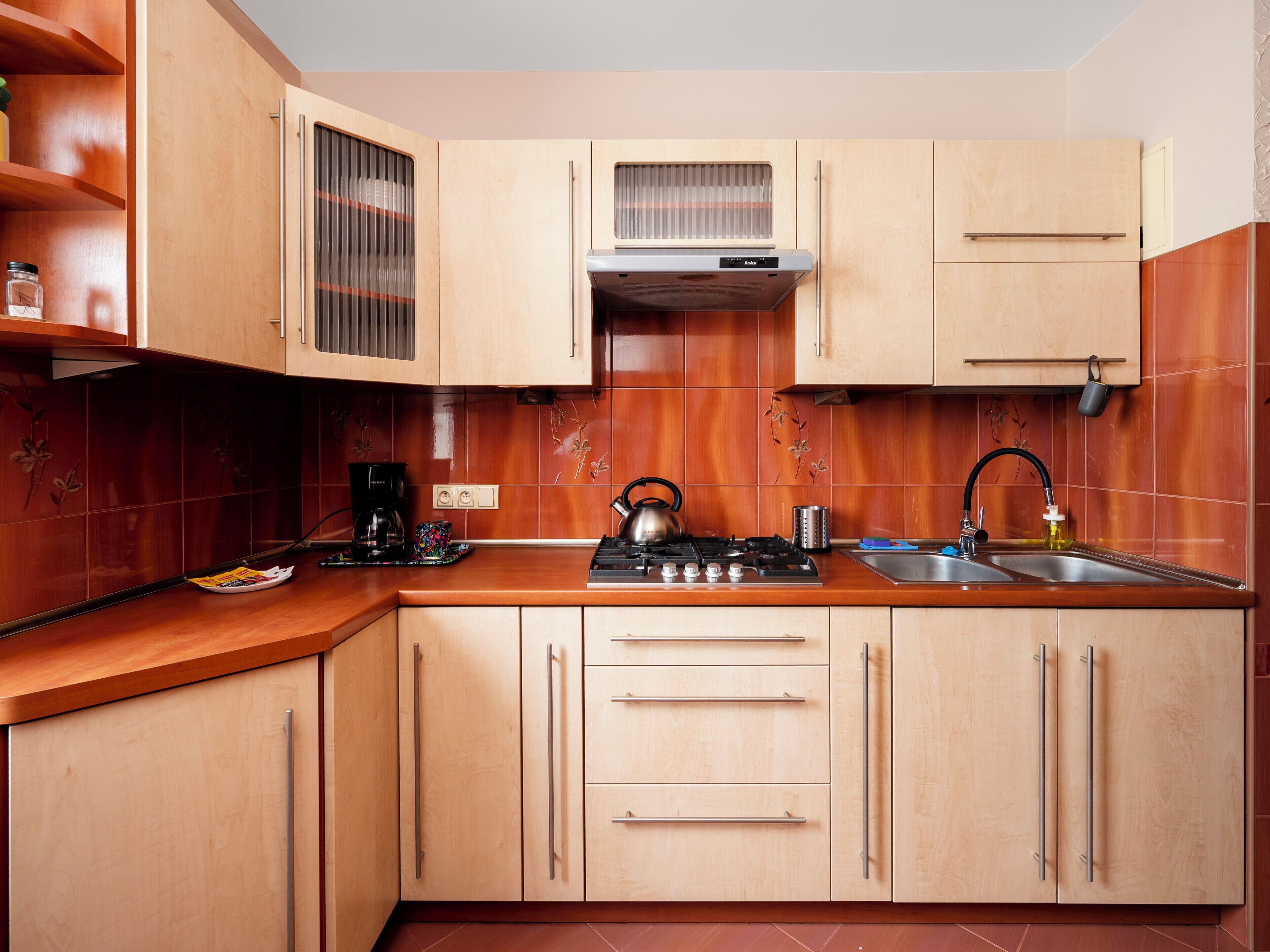 Een moderne keuken met houten kastjes, een gasfornuis, een waterkoker, een koffiezetapparaat en een spoelbak.