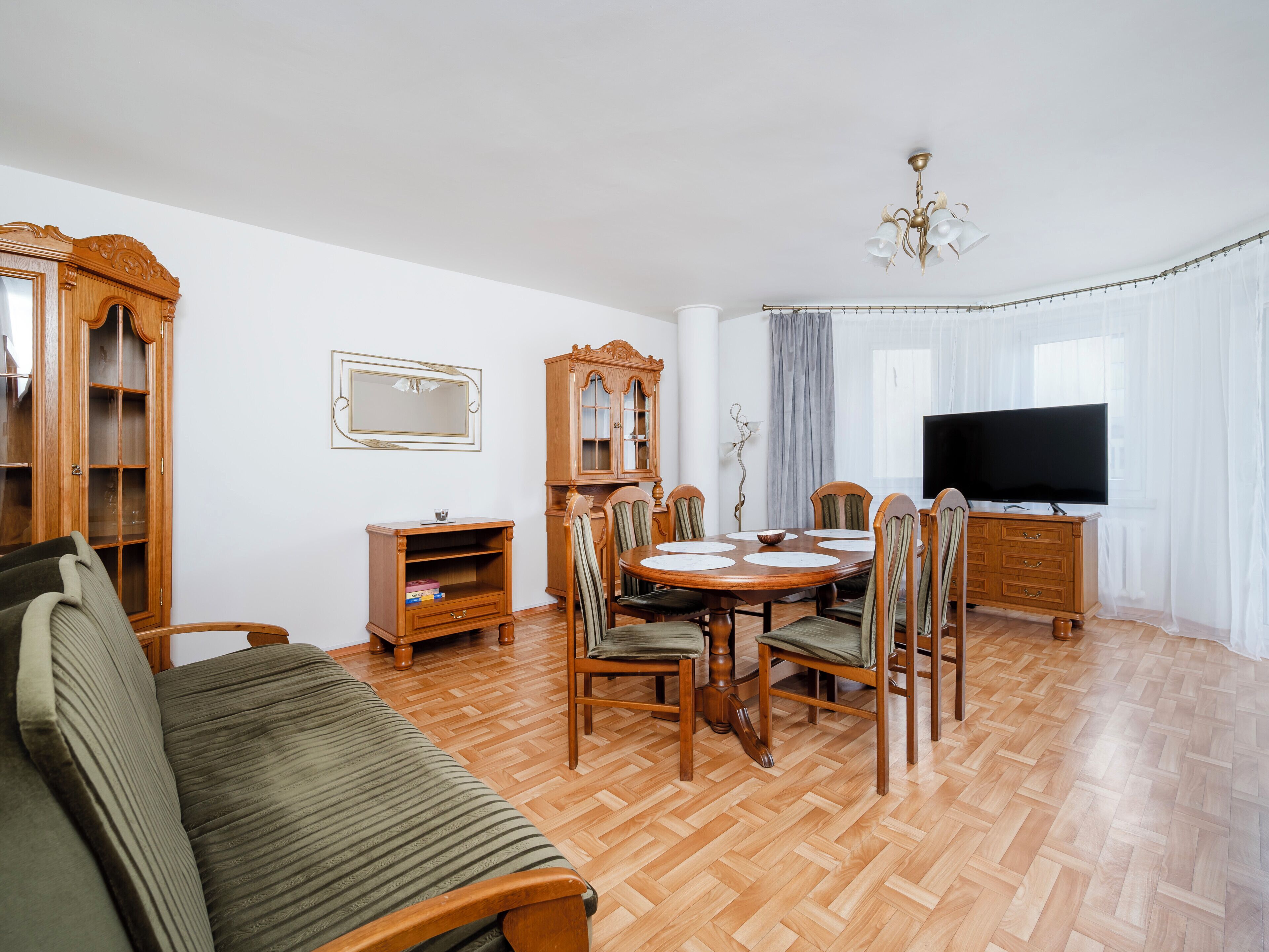 Un salon comprenant un canapé, une table à manger, des chaises, un téléviseur et un meuble en bois.