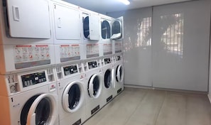 Une laverie équipée de plusieurs machines à laver et de plusieurs séchoirs, ainsi que de panneaux de commande et de panneaux d’information.