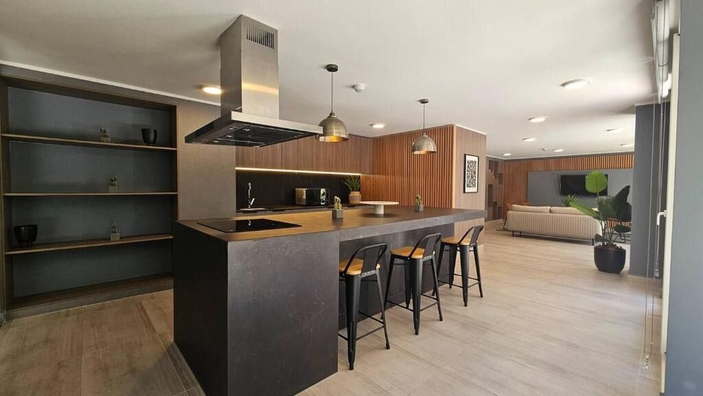 Una cocina moderna con una isla central, taburetes de bar y un área de estar con sofá y plantas.