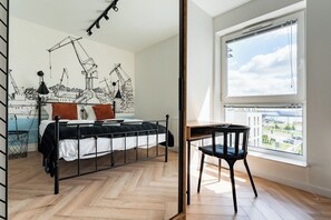 Ein Schlafzimmer mit Bett, Schreibtisch, Stuhl, Fenster und Wandbild.