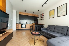 Ein modernes Wohnzimmer mit einem grauen Sofa, einem kleinen runden Tisch und einem Fernseher auf einem Holzgestell.