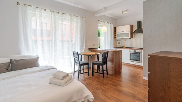 Hotellihuoneessa on sänky, pieni ruokapöytä tuoleineen, pieni keittiönurkkaus ja ikkuna, jossa on verhot.