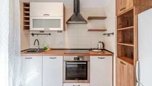 Kompakti keittiö, jossa on valkoiset kaapit, Bosch-uuni, mikroaaltouuni ja puiset hyllyt.