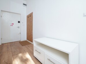Une pièce avec une porte blanche, un mur recouvert d’un panneau de liège, une armoire blanche et un plancher en bois.