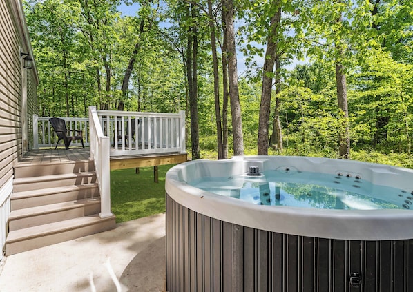 Ein Whirlpool auf einer Holzterrasse mit weißer Brüstung, umgeben von Bäumen.