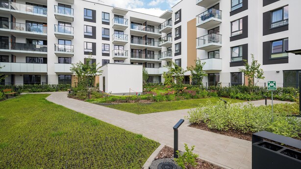 A modern apartment complex with multiple balconies, a central courtyard, and a small garden area.
