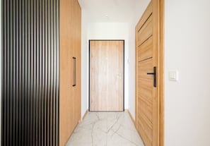 A hallway with a wooden door, a vertical striped panel, and a marble floor.