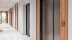 A modern hallway with a wooden panel wall, a glass door with a red sign, and an elevator.