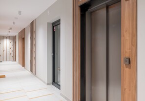 Een moderne hal met een houten paneelwand, een glazen deur met een rood bord en een lift.