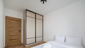 A bedroom with a wooden door, a sliding wardrobe, a bed with white linens, and a ceiling light fixture.