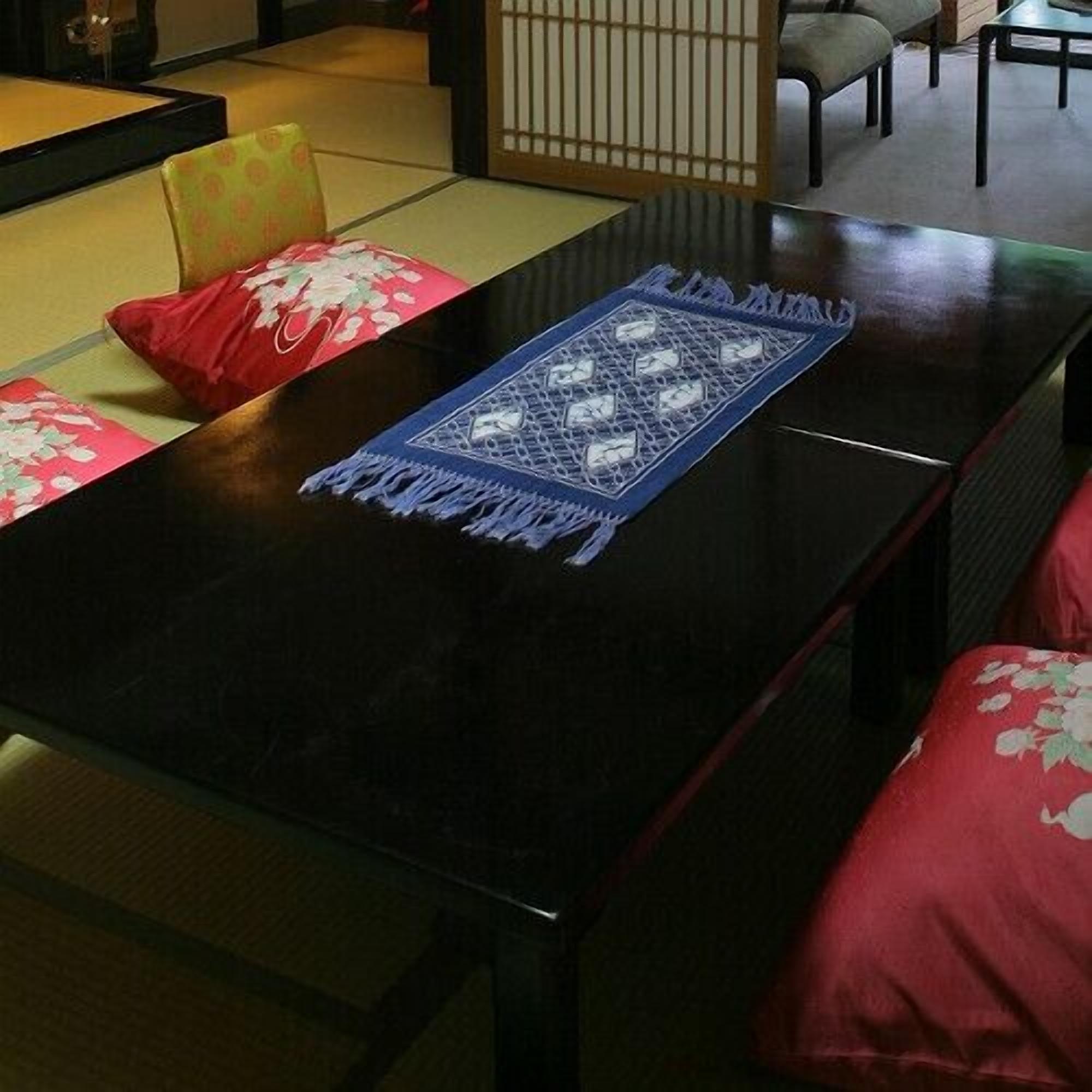 Una habitación tradicional japonesa con suelo de tatami, una mesa baja y cojines rojos.