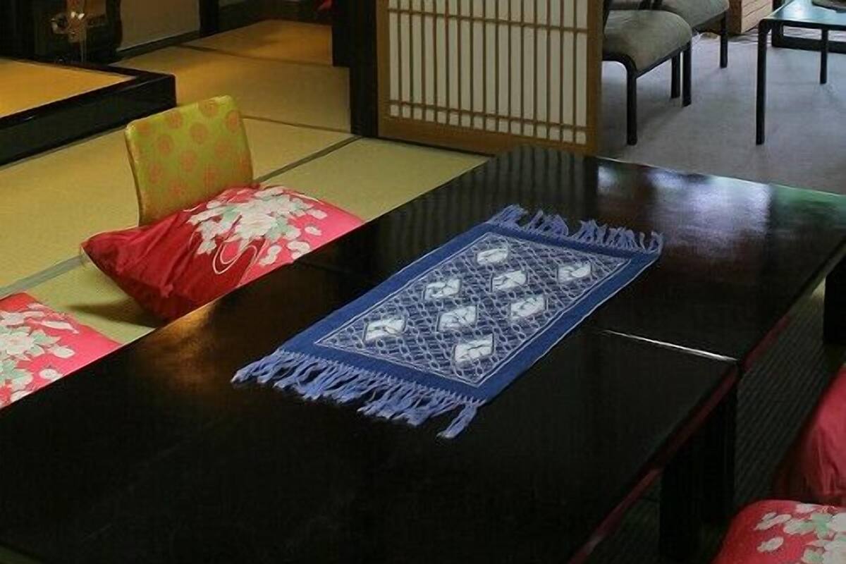 Quarto em estilo japonês tradicional com tatames, uma mesa baixa e almofadas vermelhas.
