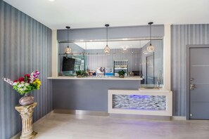 Uma área de recepção com design moderno, com balcão de atendimento, um vaso decorativo com flores e uma parede com detalhes em azulejo.
