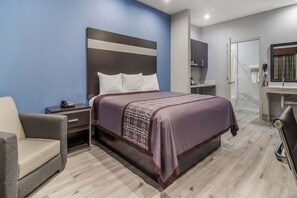 Quarto de hotel com cama, mesa de cabeceira, cadeira e banheiro com chuveiro e vaso sanitário.