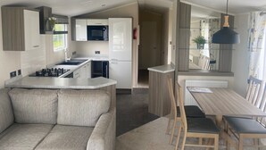 A modern kitchen with a built-in microwave, a sink, and a dining area with a table and chairs. - Ty Newydd Leisure Park 2-Bed Caravan, Sleeps 6 (Llanbedrgoch)