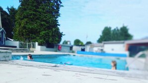 A swimming pool area with a tiled deck, a few people swimming, and trees in the background. - Ty Newydd Leisure Park 2-Bed Caravan, Sleeps 6 (Llanbedrgoch)